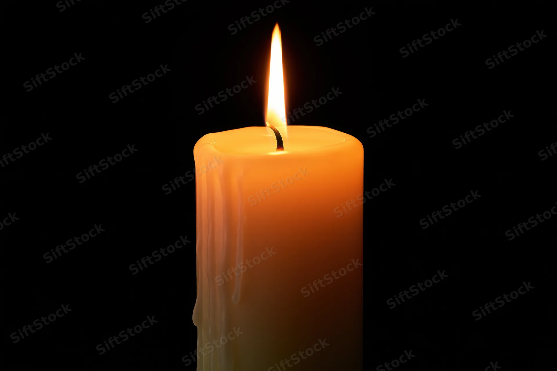 A lit ivory pillar candle burning steadily against a black background