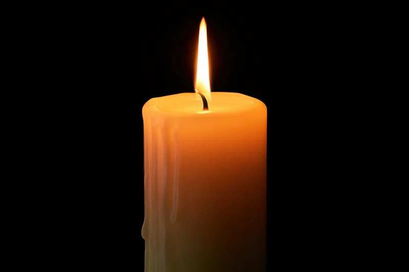 A lit ivory pillar candle burning steadily against a black background