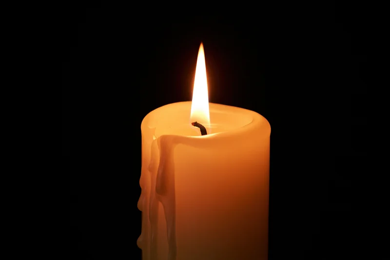 A lit ivory pillar candle burning steadily against a pure black background