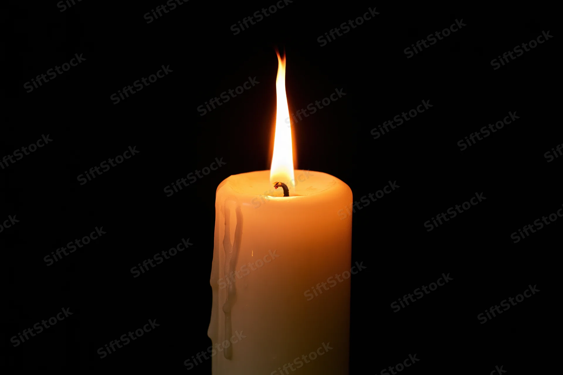 A single ivory pillar candle burning steadily against a pure black background