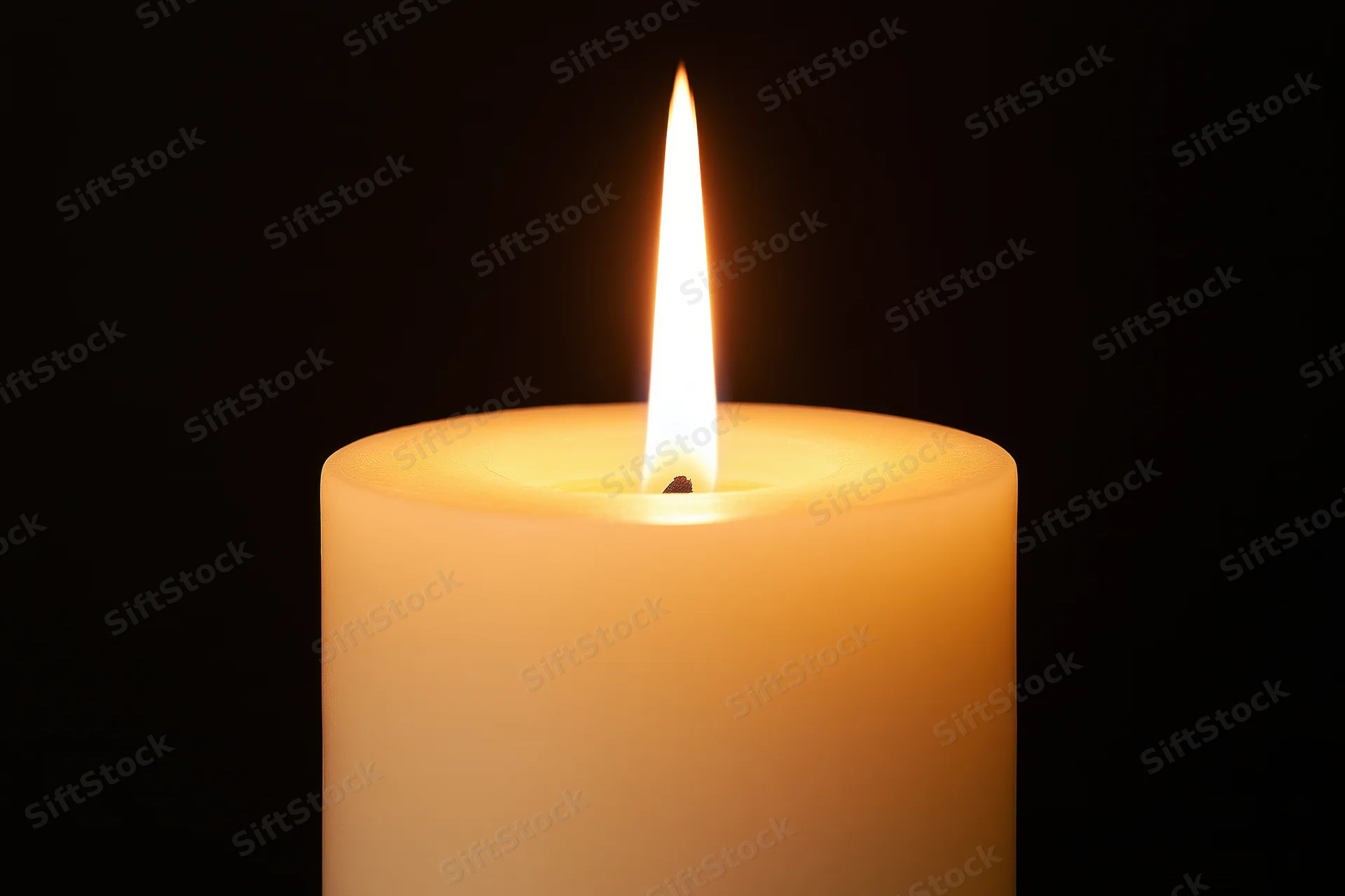 Ivory pillar candle burning with steady flame against dark background