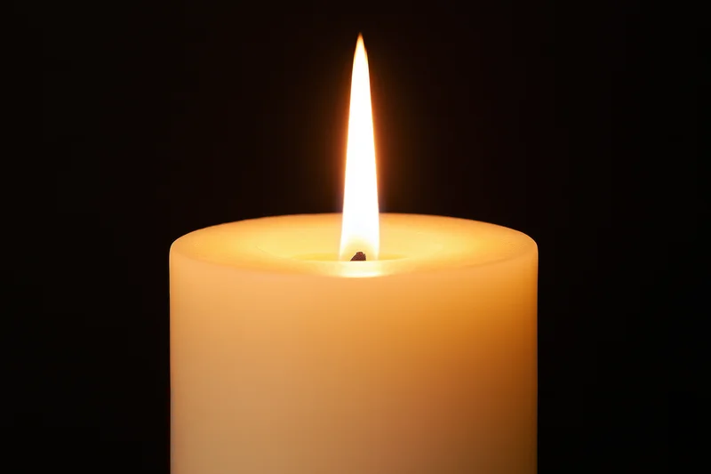 Ivory pillar candle burning with steady flame against dark background