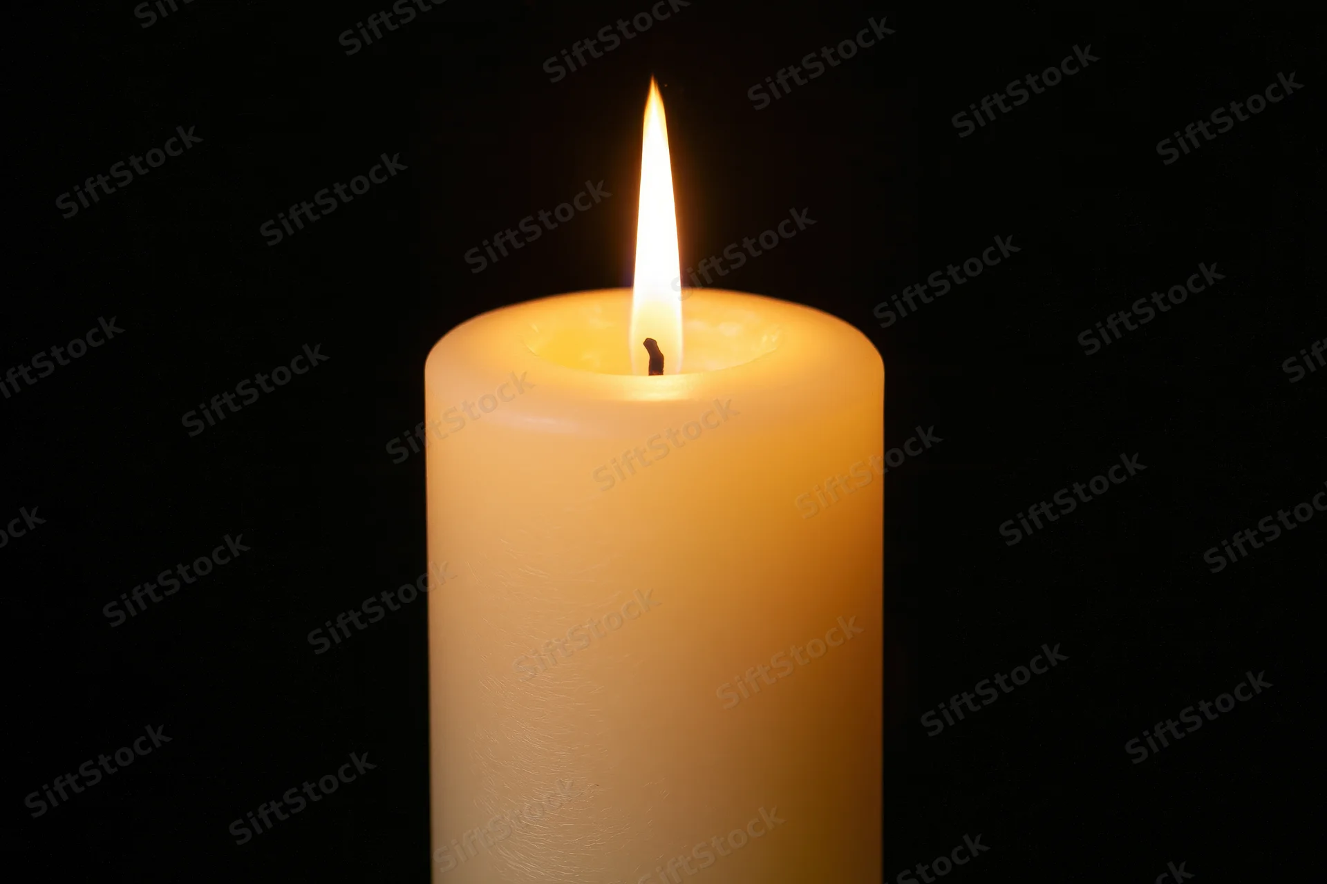 Ivory pillar candle burning with steady flame against black background