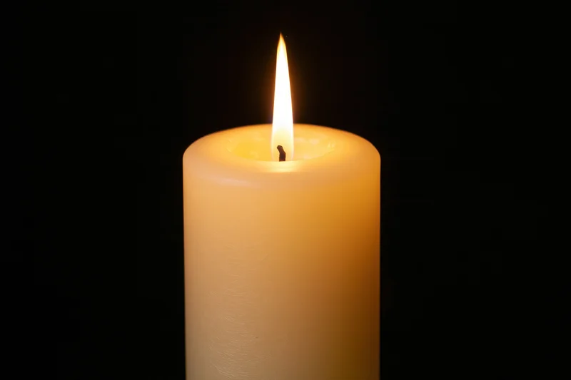Ivory pillar candle burning with steady flame against black background