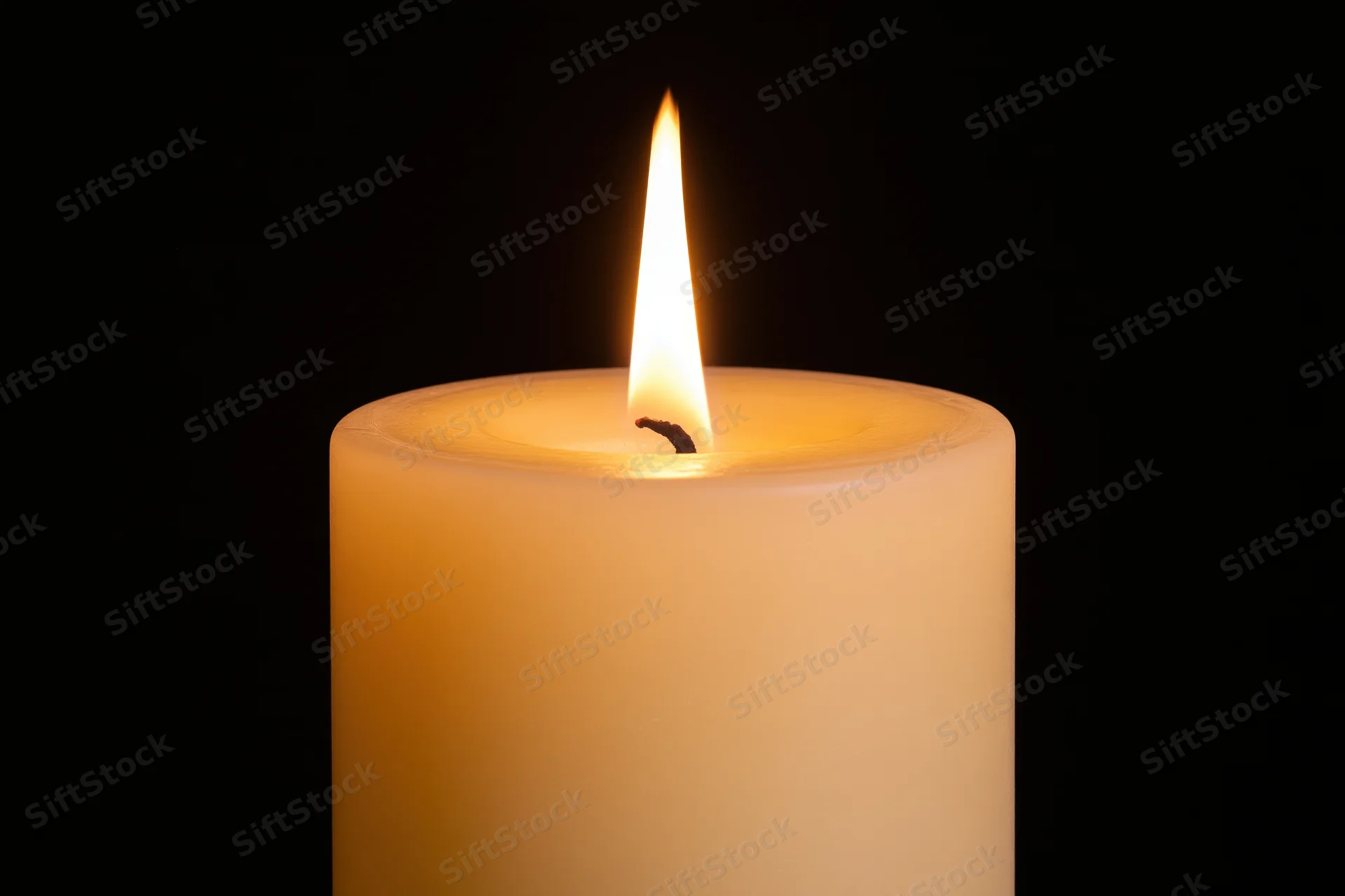 Ivory pillar candle burning with steady flame against black background