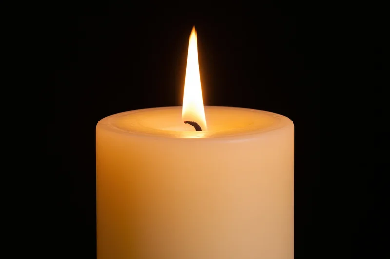 Ivory pillar candle burning with steady flame against black background