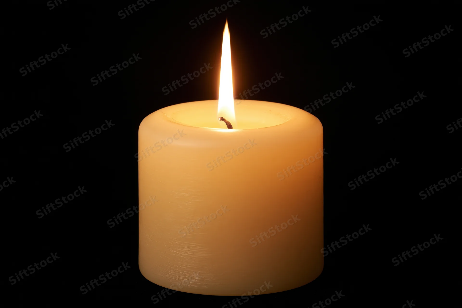 Ivory pillar candle burning with steady flame against black background
