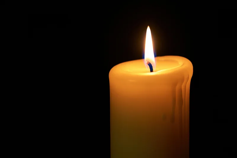 Lit candle burning against a black background with warm glow and melted wax