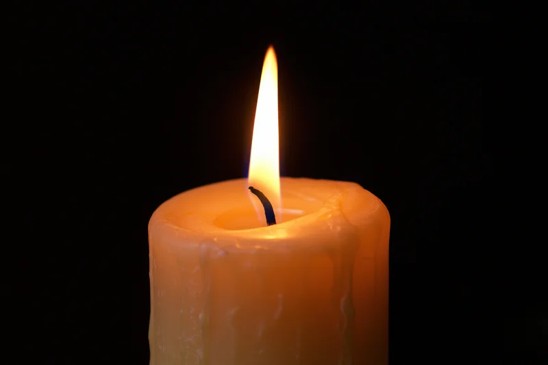 Lit candle burning with a steady flame against a pure black background