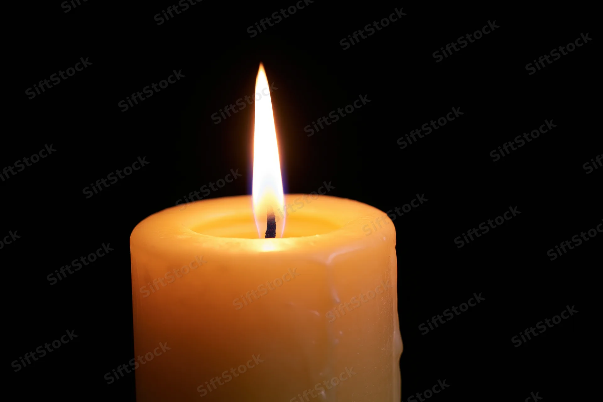 Lit candle burning with flame centered against black background