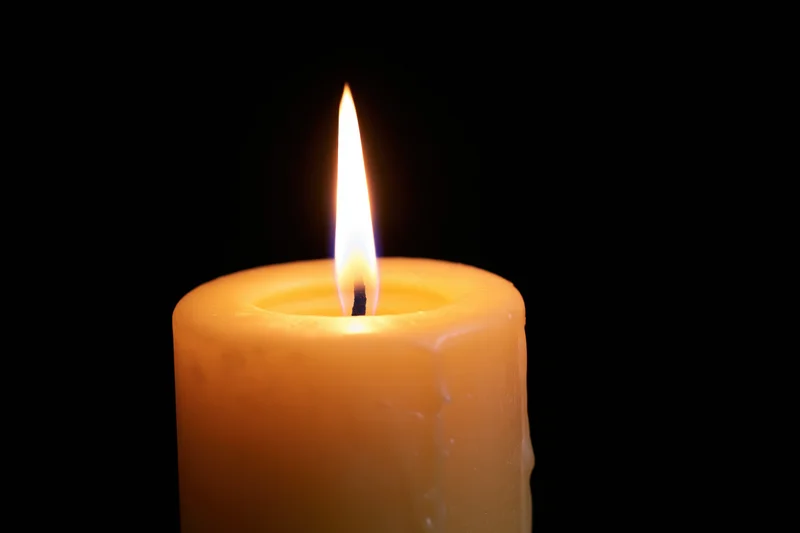 Lit candle burning with flame centered against black background