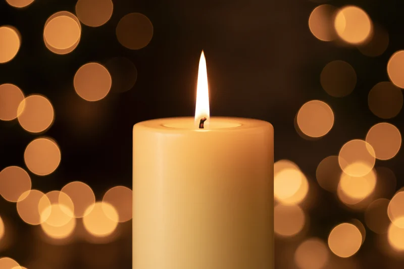 A lit pillar candle with a steady flame against a warm bokeh background