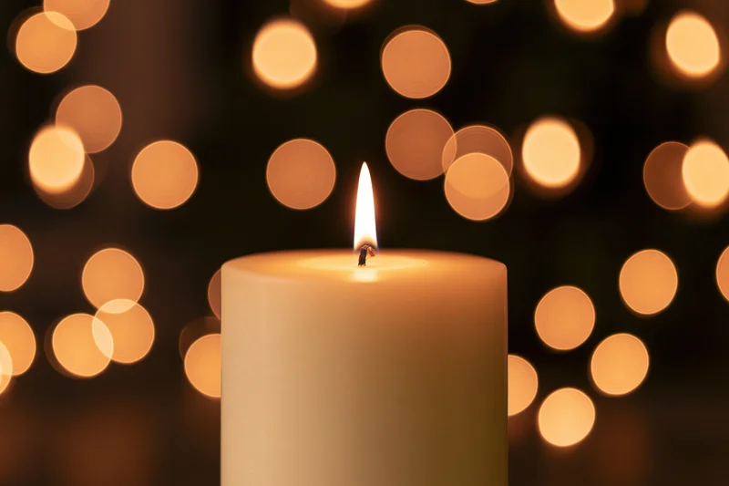 Single white pillar candle burning with steady flame against blurred warm bokeh lights