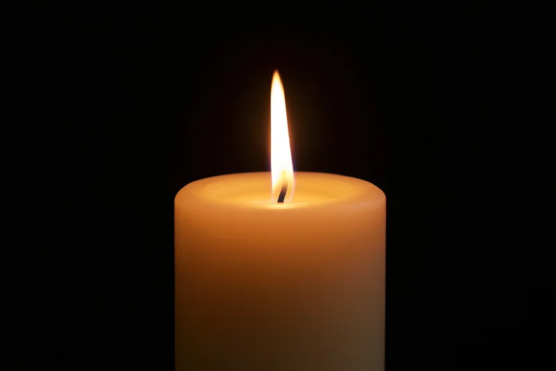 Single pillar candle burning with steady flame centered against black background