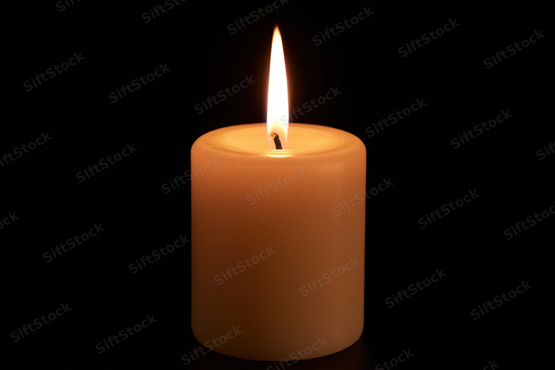 Single pillar candle burning with steady flame centered against black background