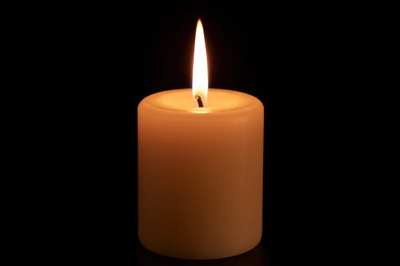 Single pillar candle burning with steady flame centered against black background