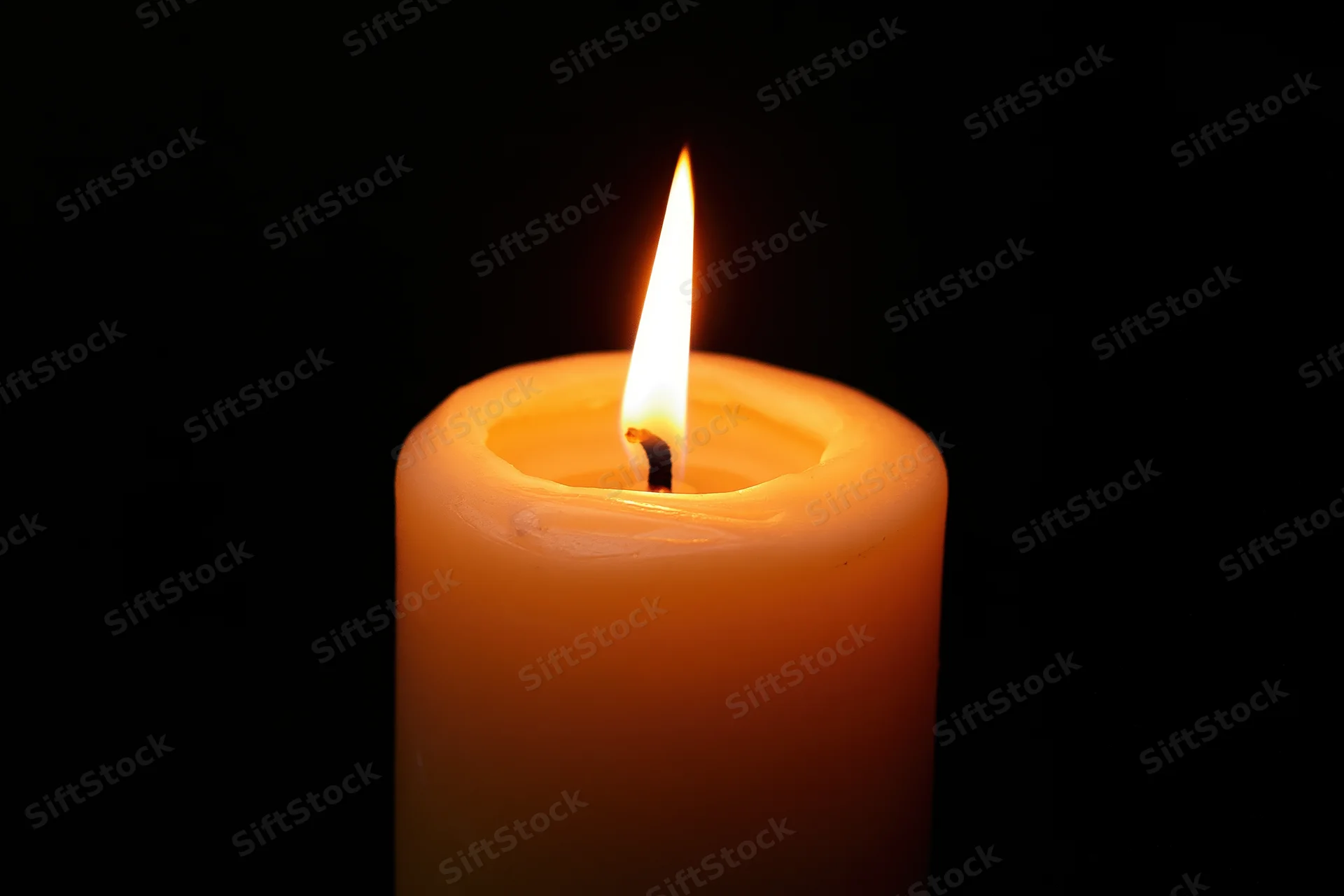 Single pillar candle burning with steady flame centered against black background
