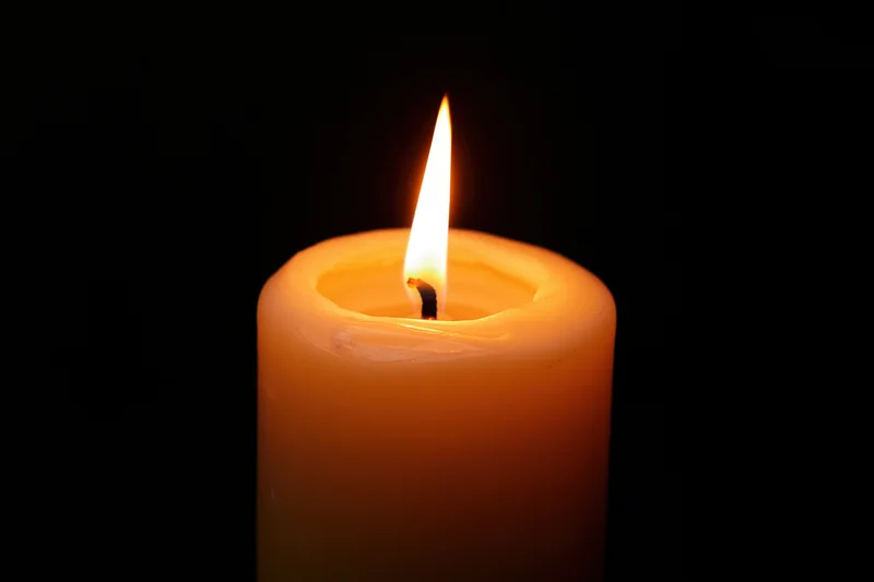 Single pillar candle burning with steady flame centered against black background