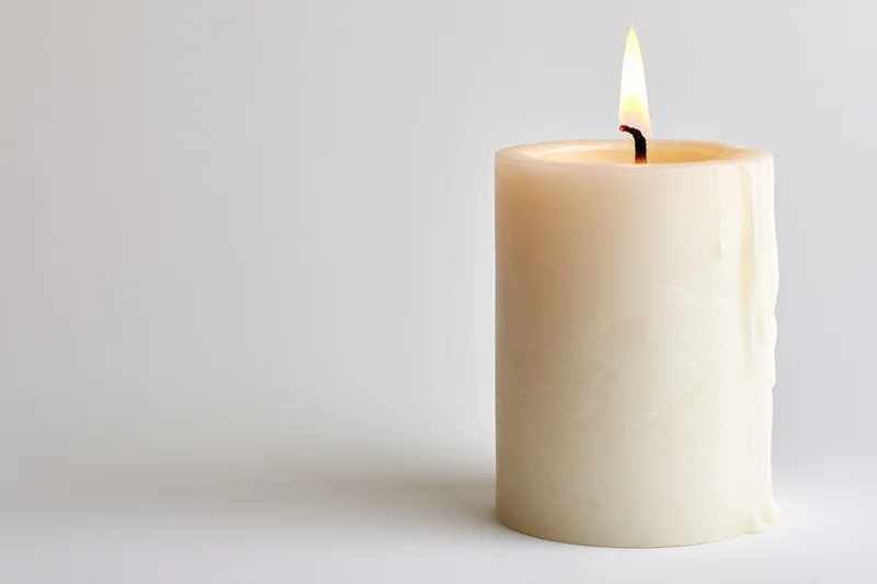 White pillar candle burning with steady flame on plain background