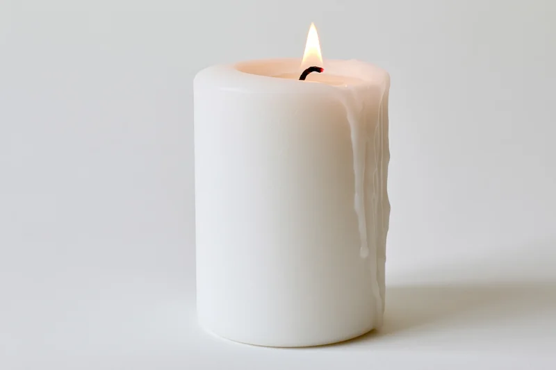 White pillar candle burning with a steady flame on a plain white surface