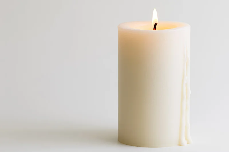 White pillar candle burning with a steady flame on a plain white surface