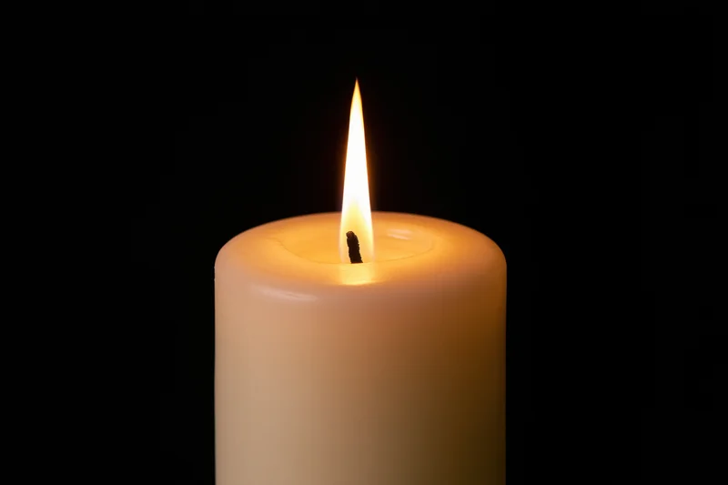 White pillar candle burning with a tall steady flame against black background