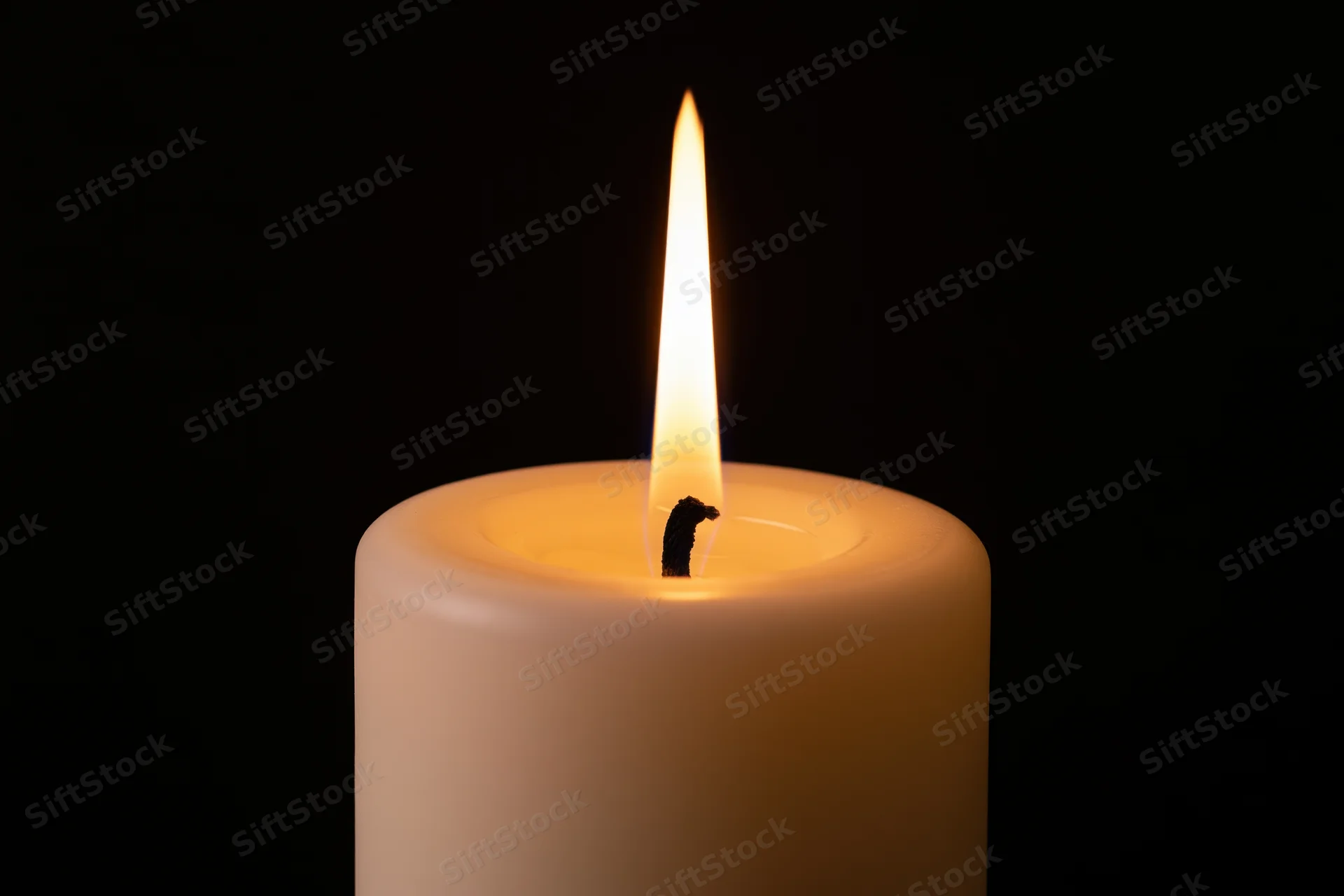 White pillar candle burning with tall steady flame against black background