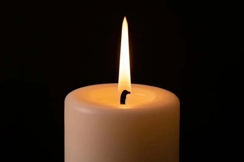 White pillar candle burning with tall steady flame against black background