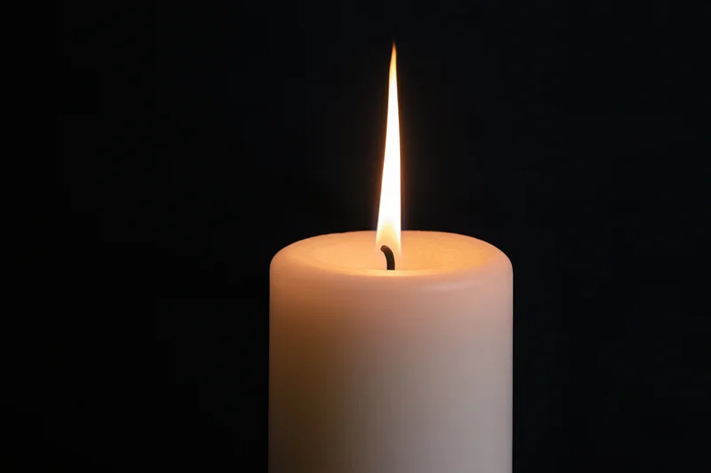 White pillar candle burning with a tall steady flame against black background