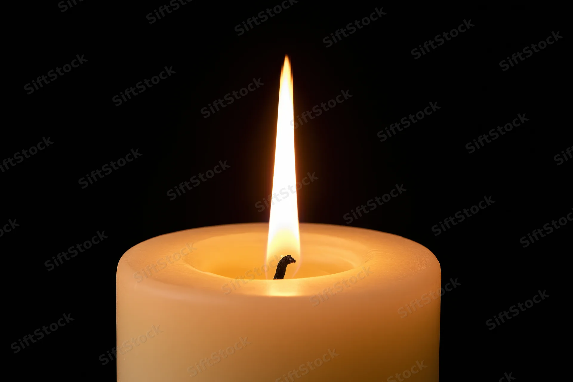 White pillar candle burning with tall steady flame against black background