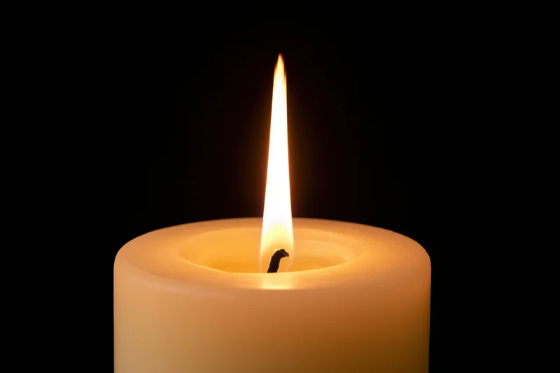 White pillar candle burning with tall steady flame against black background