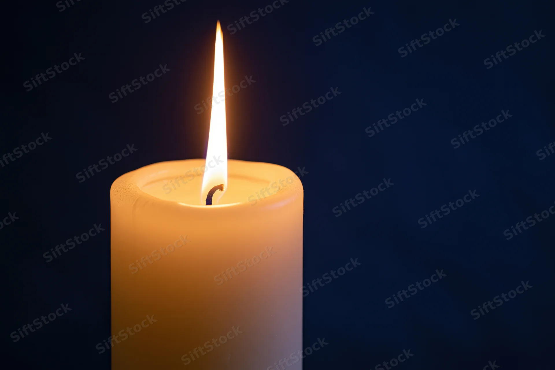 White pillar candle burning with a tall steady flame against dark background