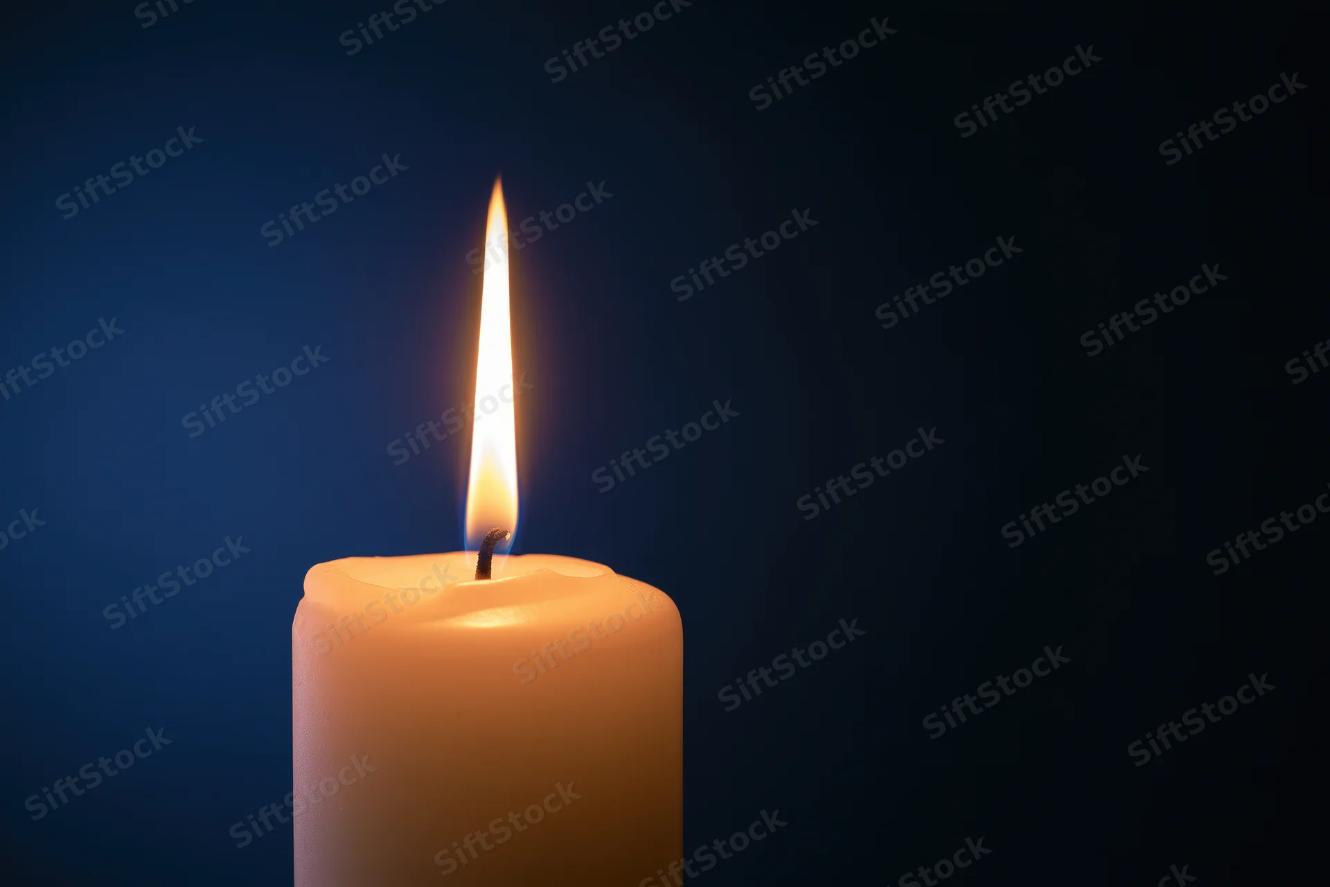 Single white pillar candle burning with a tall steady flame against a dark blue background