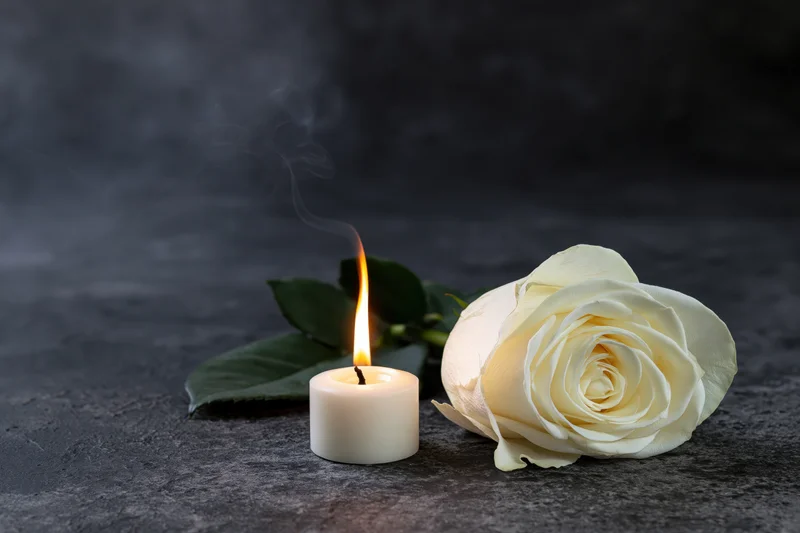White rose beside a lit candle on dark stone surface