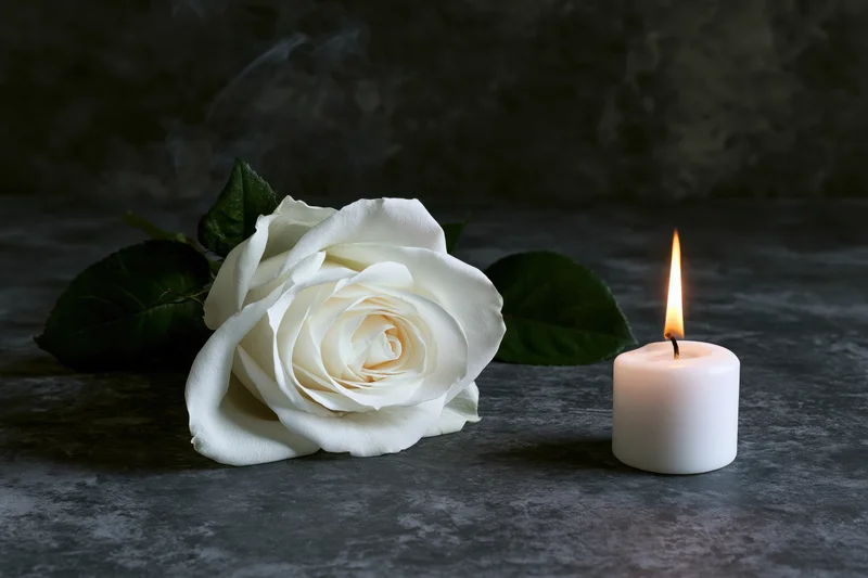 White rose lying beside a lit candle on a dark stone surface