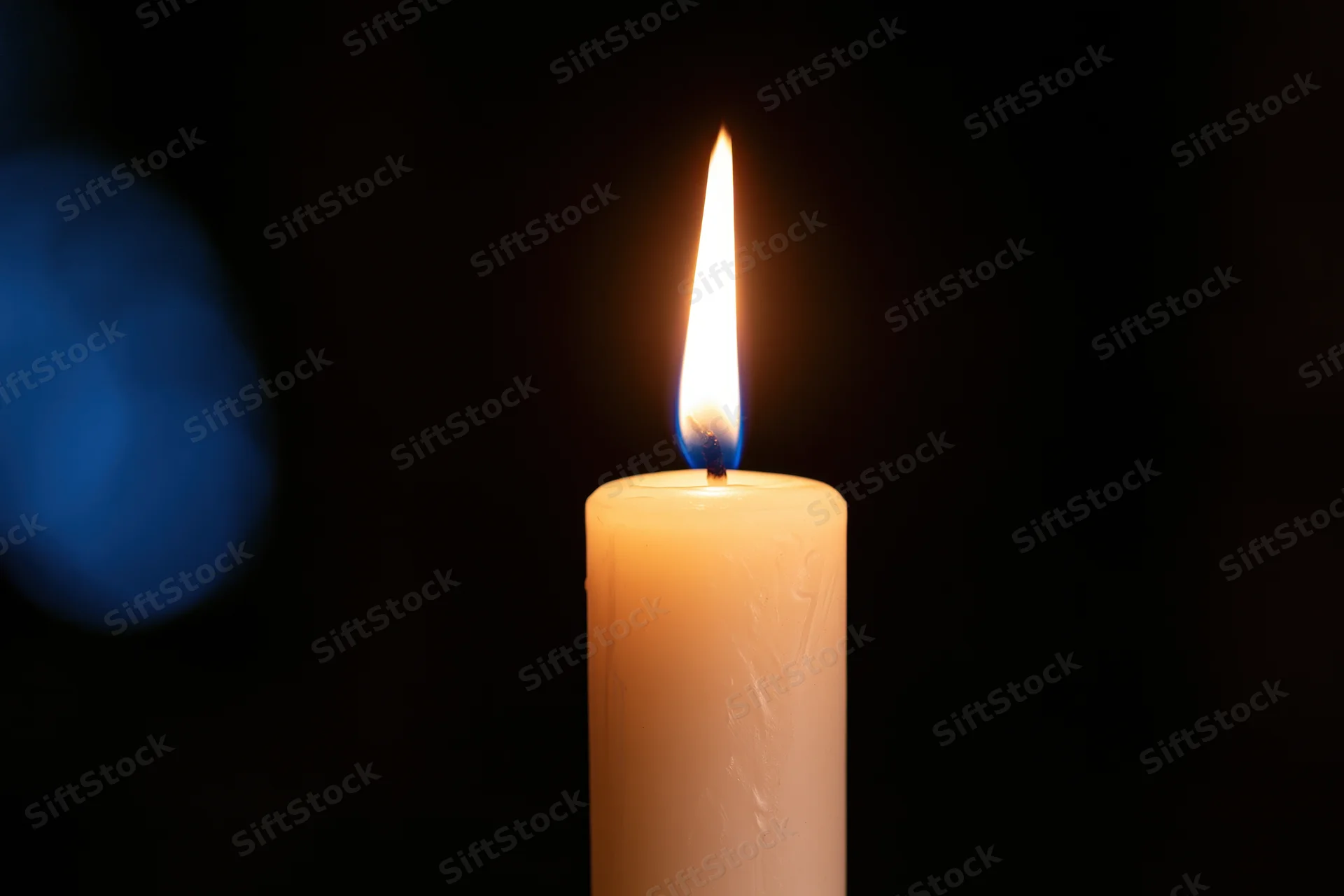 A single white taper candle burning with a steady warm flame against a dark background