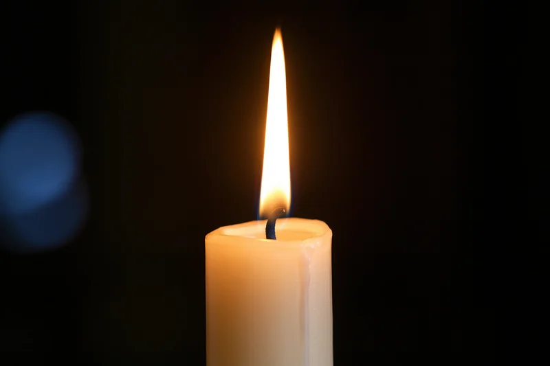 A white taper candle burning with a steady warm flame against a dark background