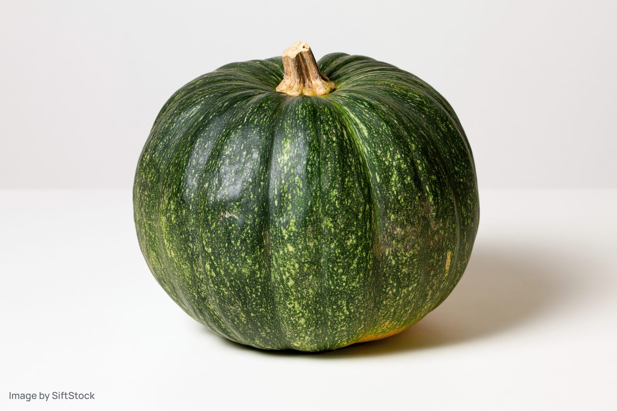 Whole kabocha squash on white surface with soft shadow