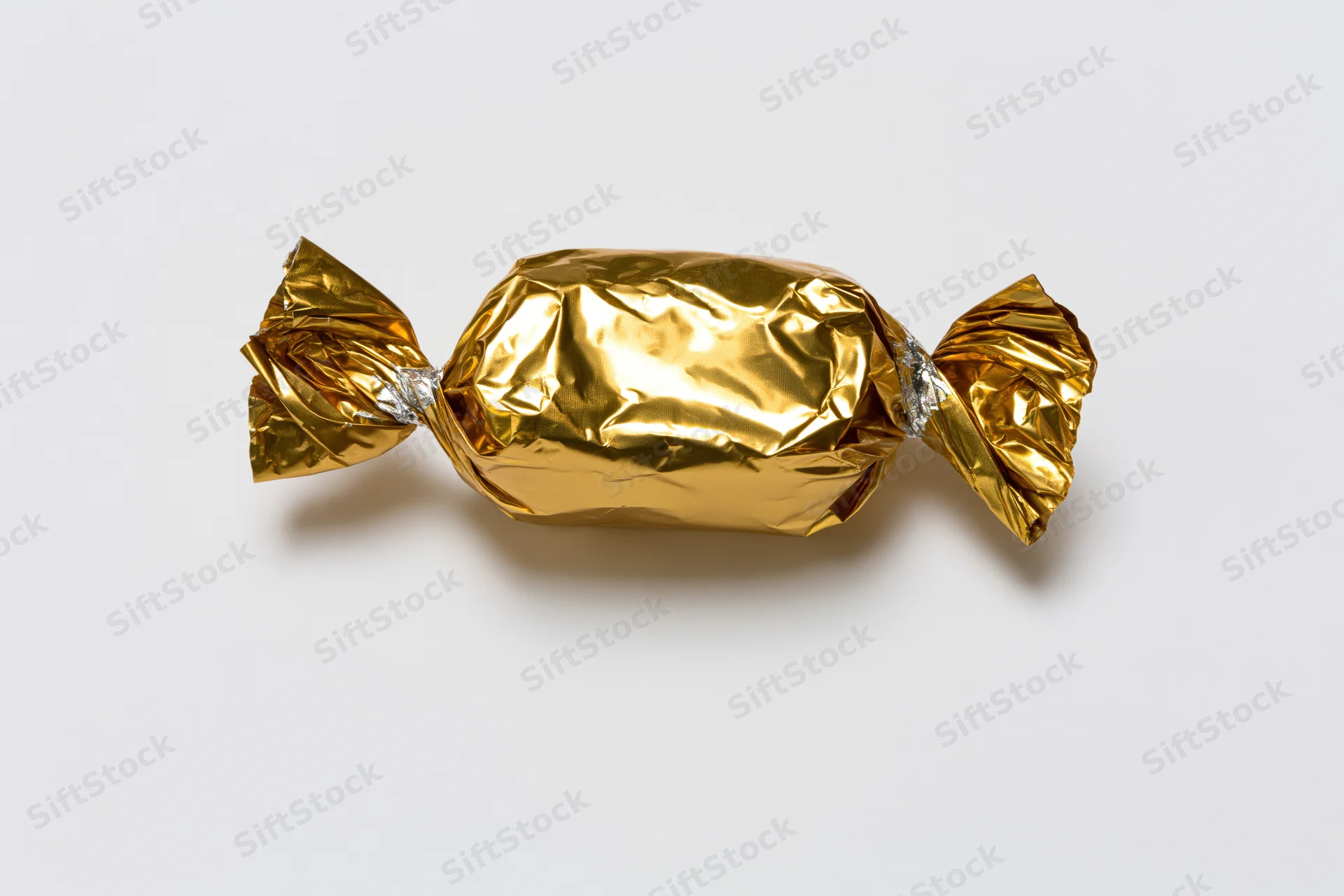 Single candy wrapped in crinkled gold foil with twisted ends on white background