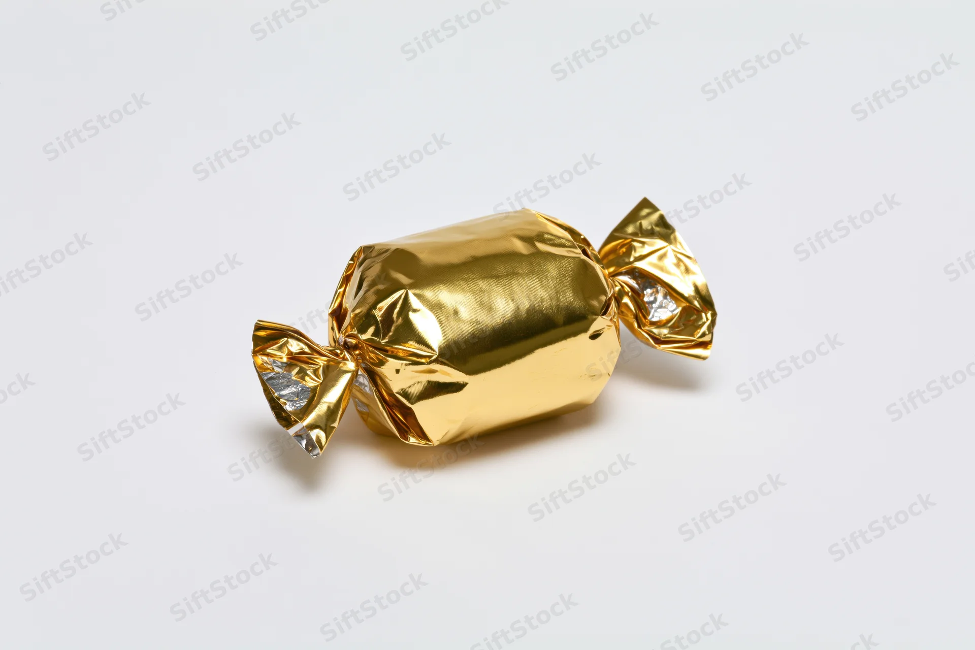 Single candy wrapped in crinkled gold foil with twisted ends on white background