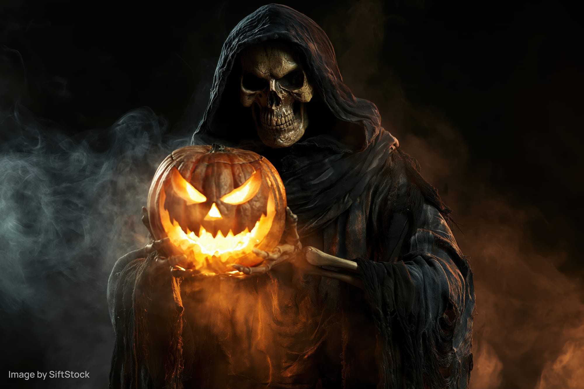 Skeletal figure in dark hooded robe holding glowing carved pumpkin in smoky night
