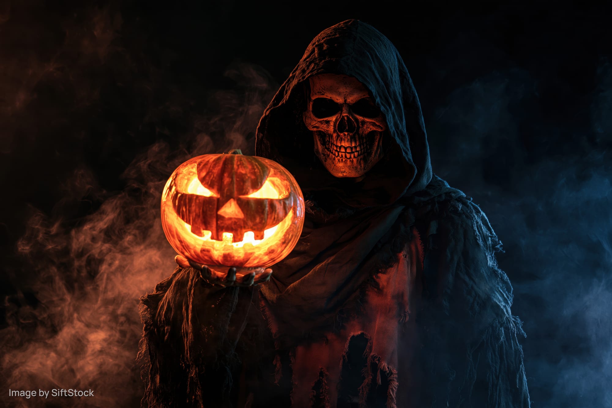 Skeletal figure in tattered hooded robe holding glowing carved pumpkin in smoky dark setting