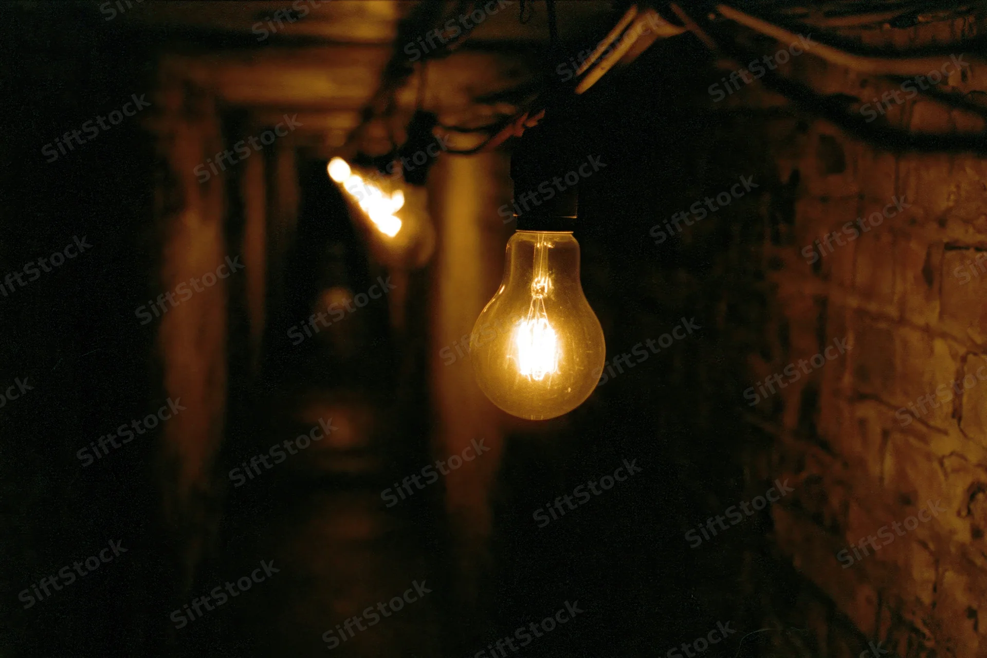 Glowing incandescent bulbs hanging in a narrow dimly lit brick tunnel