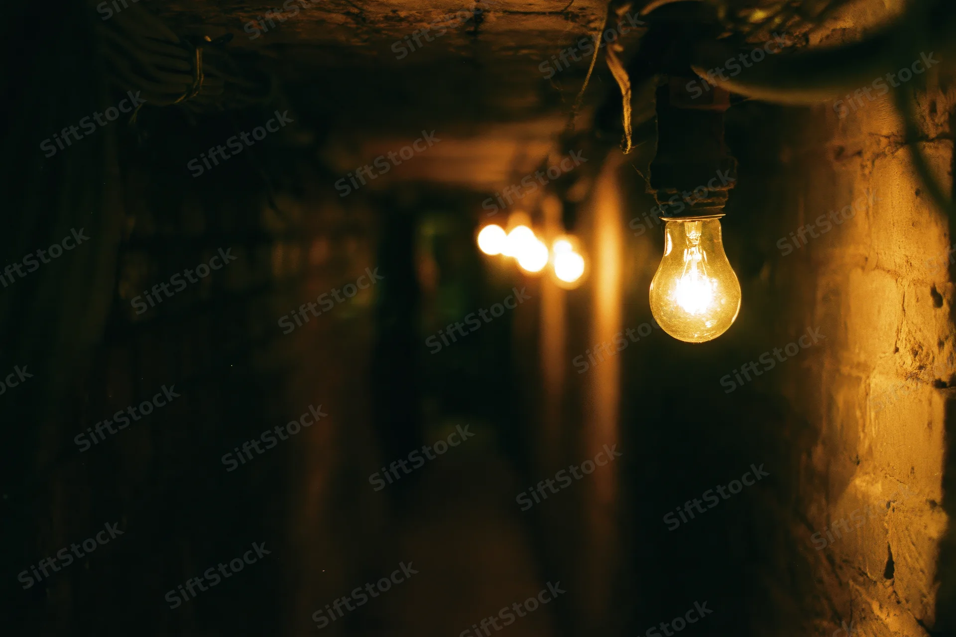 String of bare incandescent bulbs glowing in a narrow dim brick tunnel