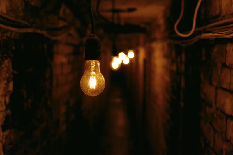 Bare incandescent bulbs hanging in a narrow brick tunnel with warm glow