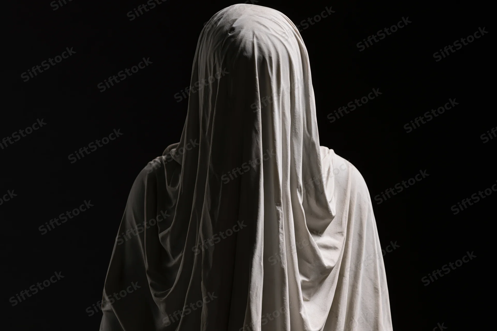 Veiled marble statue standing with head bowed against black background
