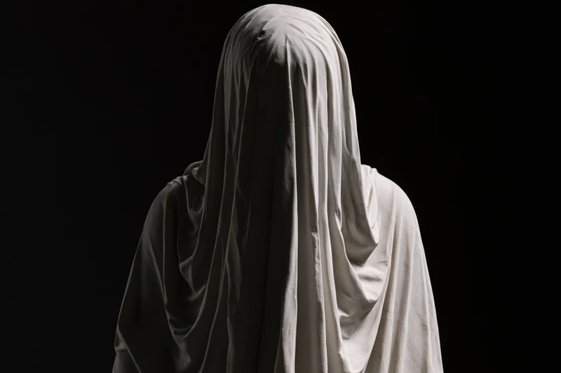 Veiled marble statue standing with head bowed against black background