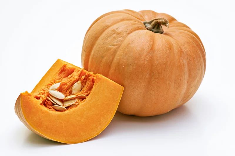 Whole pumpkin with a slice cut out and placed in front on white background