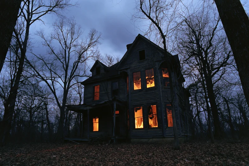Abandoned victorian house with glowing amber light in forest at night