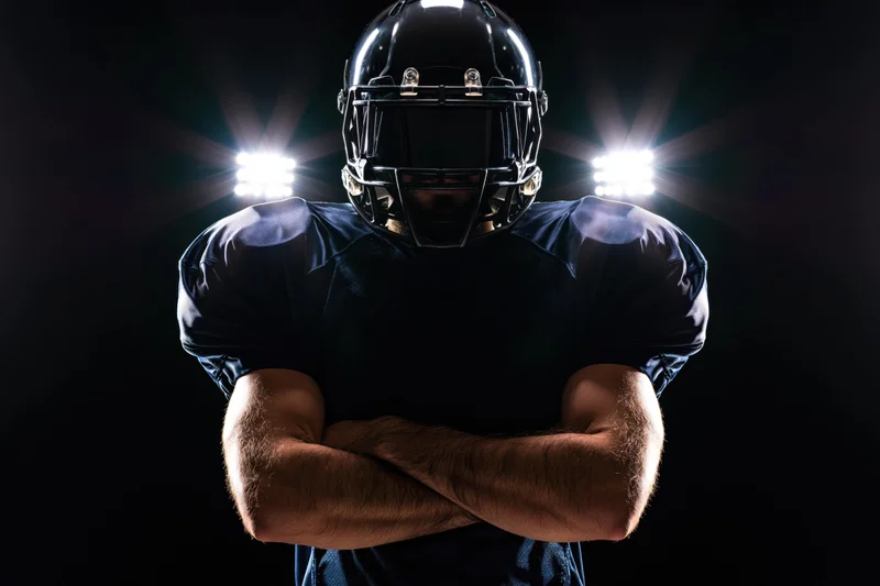 American football player with arms crossed under spotlight in dark studio